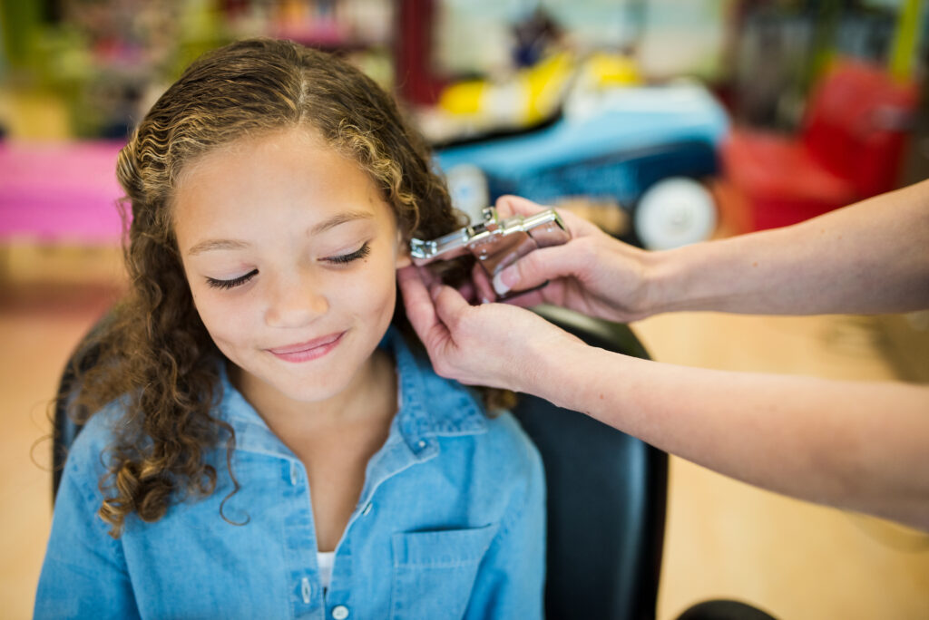 Smiling girl gets her ear pierced - Pigtails & Crewcuts Buckhead