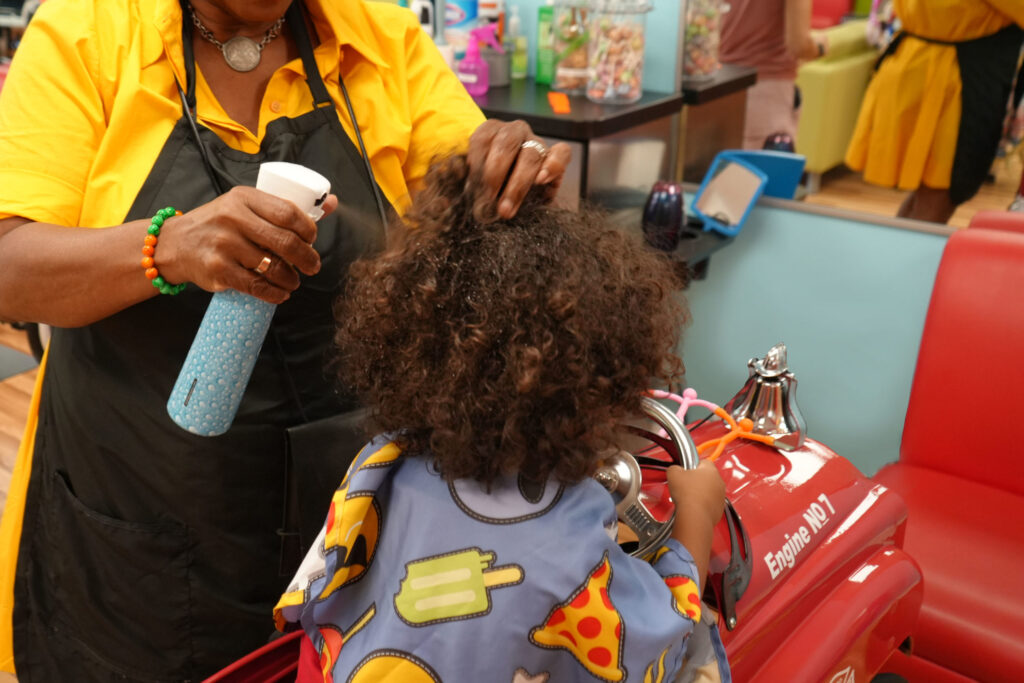 A girl with natural curly hair getting her hair styled at Pigtails & Crewcuts.