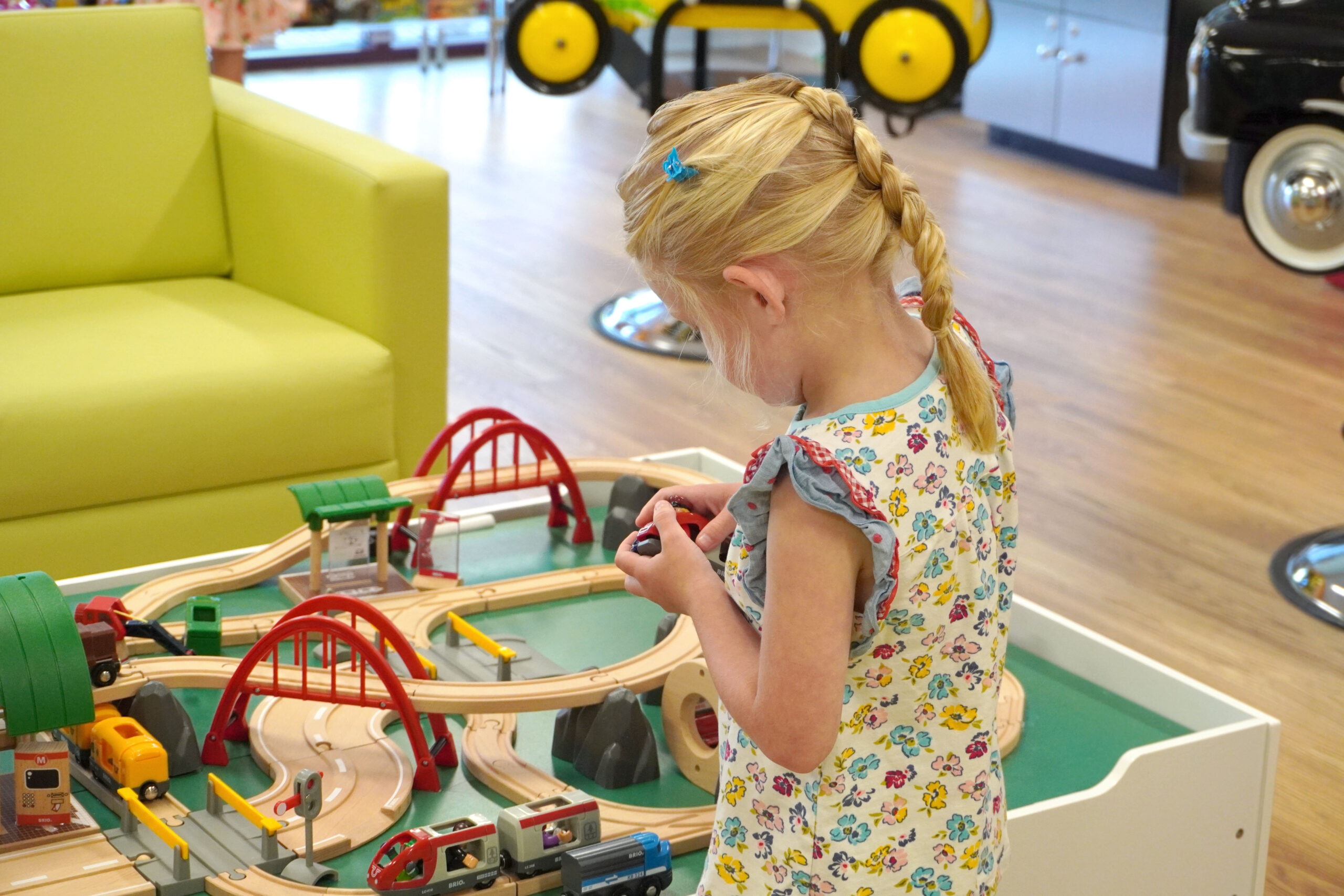 A blonde girl with a fun braid playing at the train table at Pigtails & Crewcuts Buckhead.