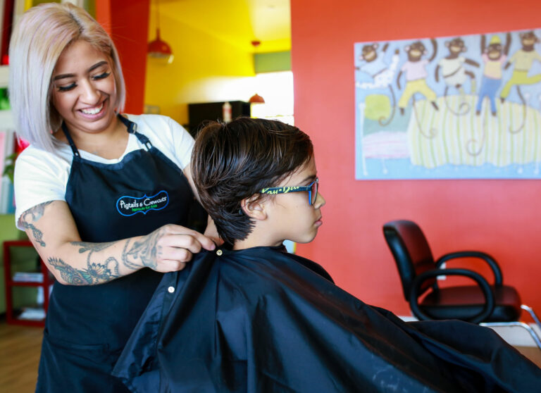 Pigtails & Crewcuts hair stylist putting a gown on a boy