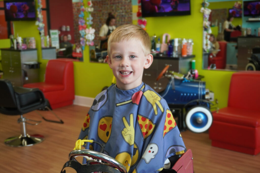 Smiling blonde boy enjoying his new haircut at Pigtails & Crewcuts East Cobb.