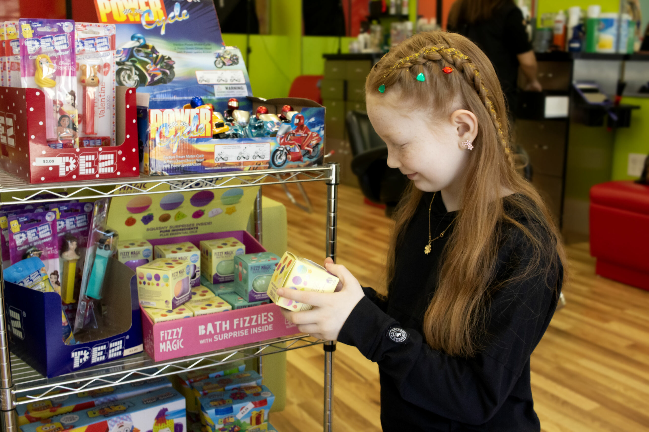 Little girl with ear piercing looking at toys - Pigtails & Crewcuts Five Forks