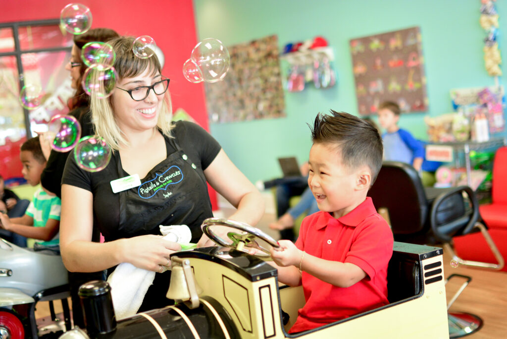 Smiling boy in themed car looks at bubbles - Pigtails & Crewcuts Jacksonville
