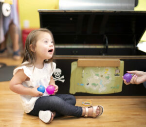 Little girl sitting and playing with toy balls - Pigtails & Crewcuts Jacksonville