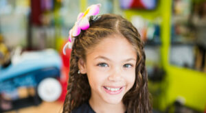 Smiling girl with flower in her hair - Pigtails & Crewcuts Jacksonville