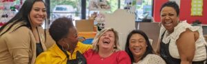 Five smiling Pigtails & Crewcuts East Memphis team members sharing a laugh inside the children’s hair salon.